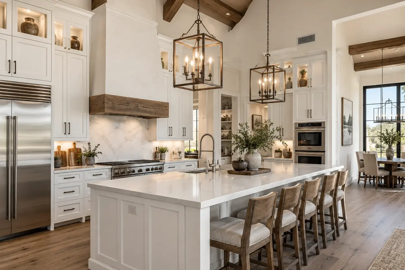 A large open-plan kitchen with white cabinetry, a marble island and lantern pendants.