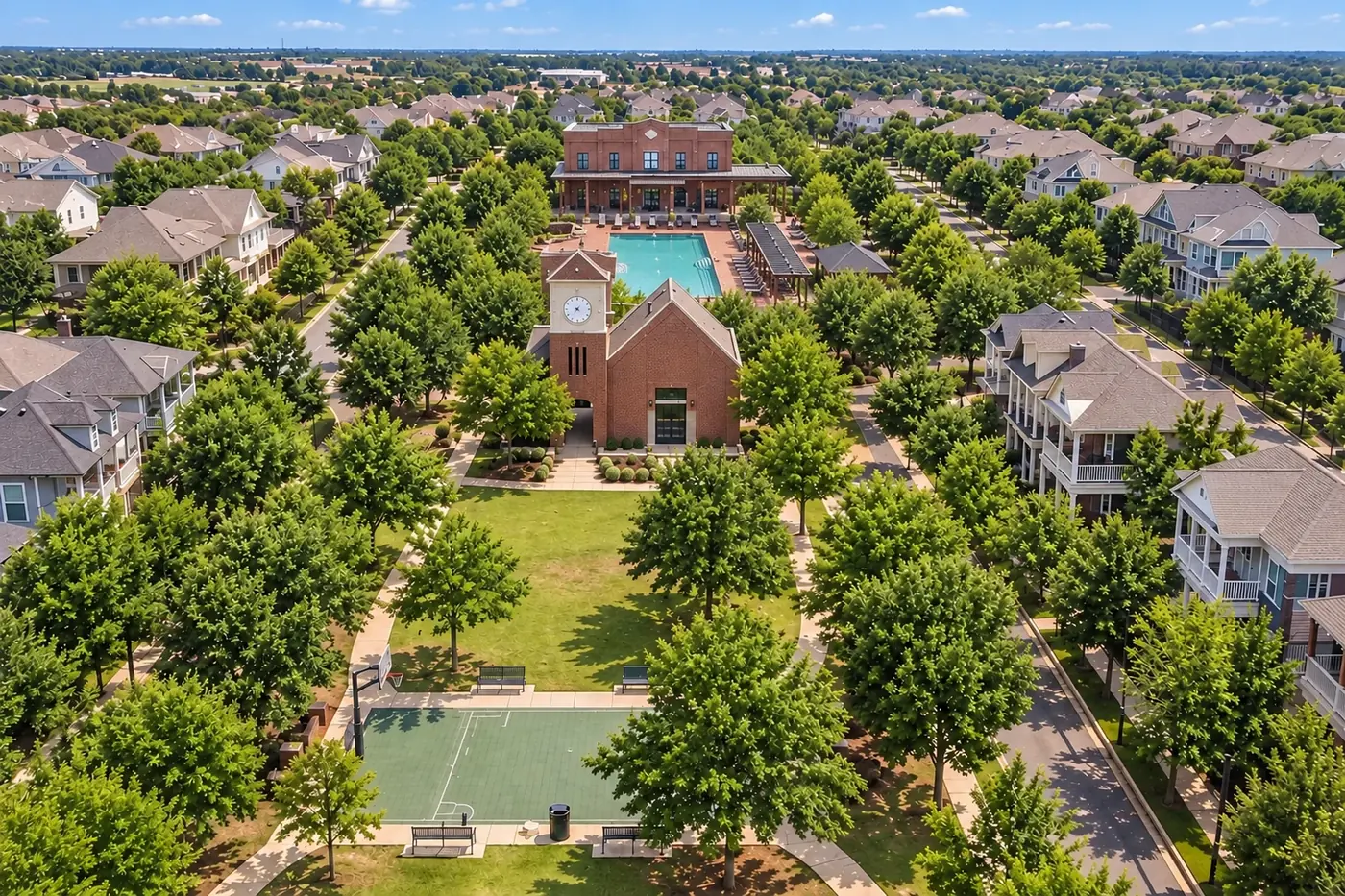 An aerial view of a neighborhood square with a clock tower, pool and shaded green.
