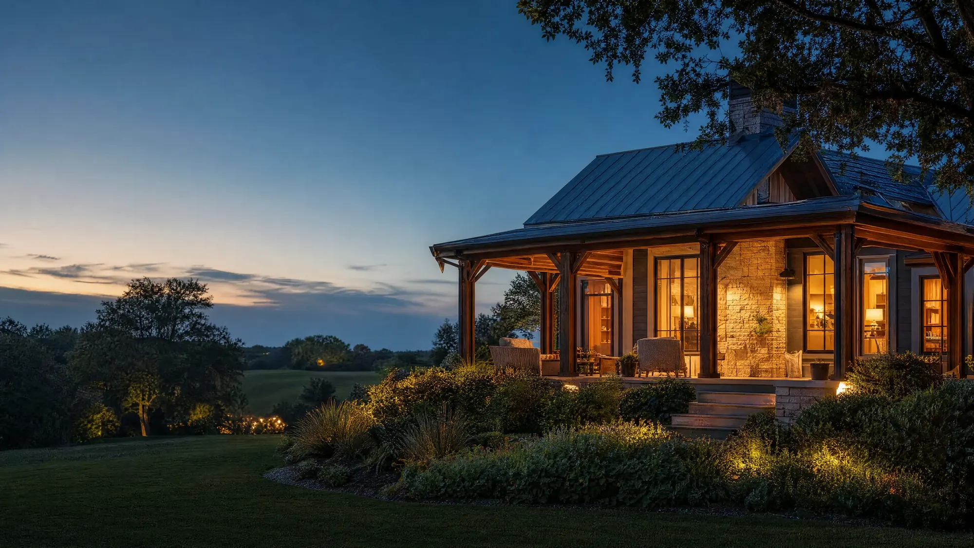 A timber and stone porch home at blue hour, warm lamps in the windows and a planted garden below.